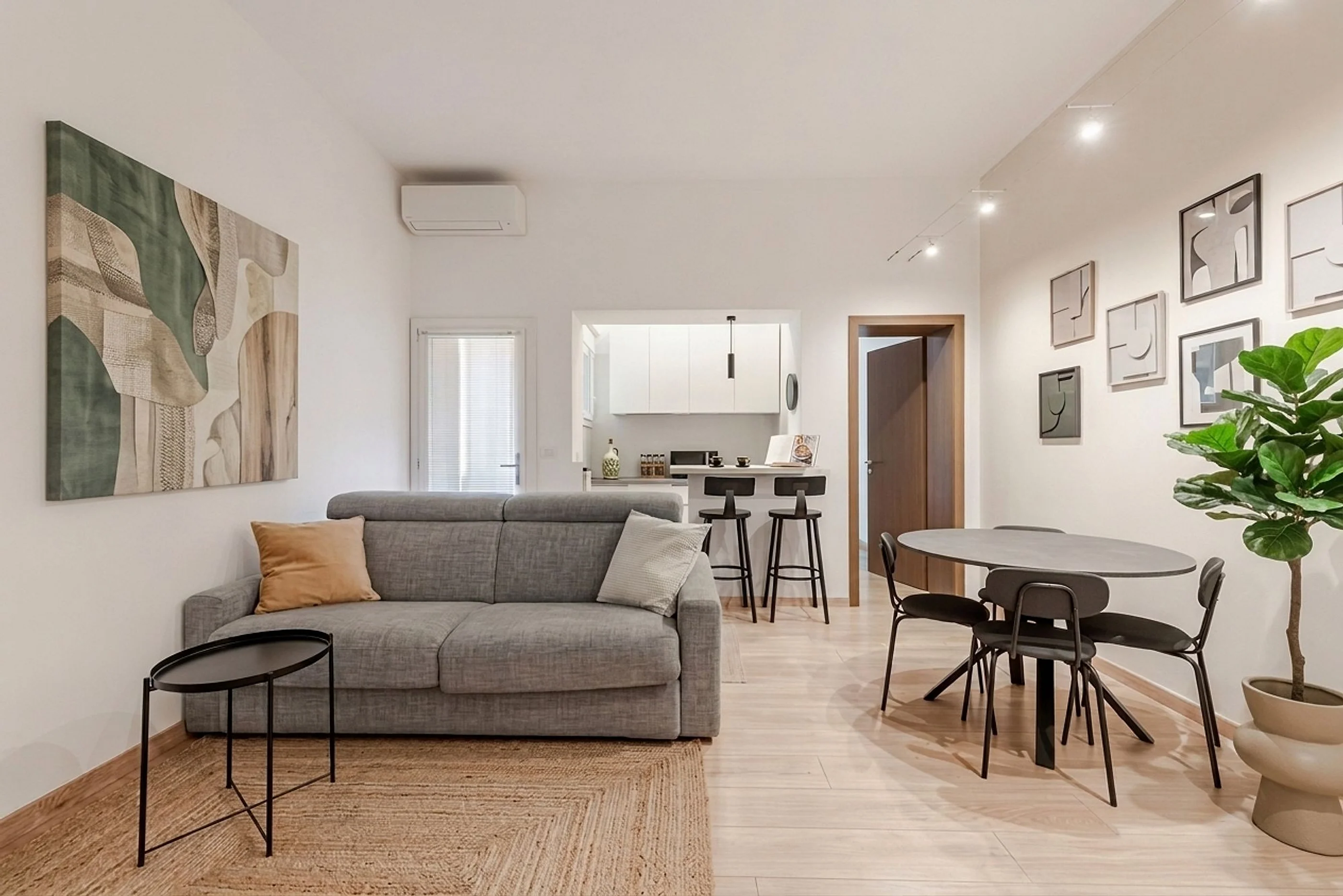 Soggiorno luminoso con divano grigio, tavolo rotondo e cucina a vista, in un appartamento a Trieste